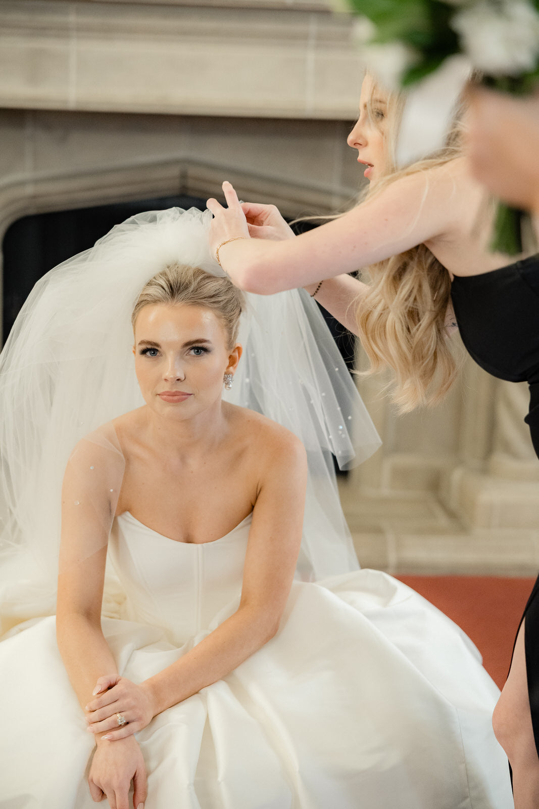 Bride sitting adjusting puffy and four layer veil in an indoor setting