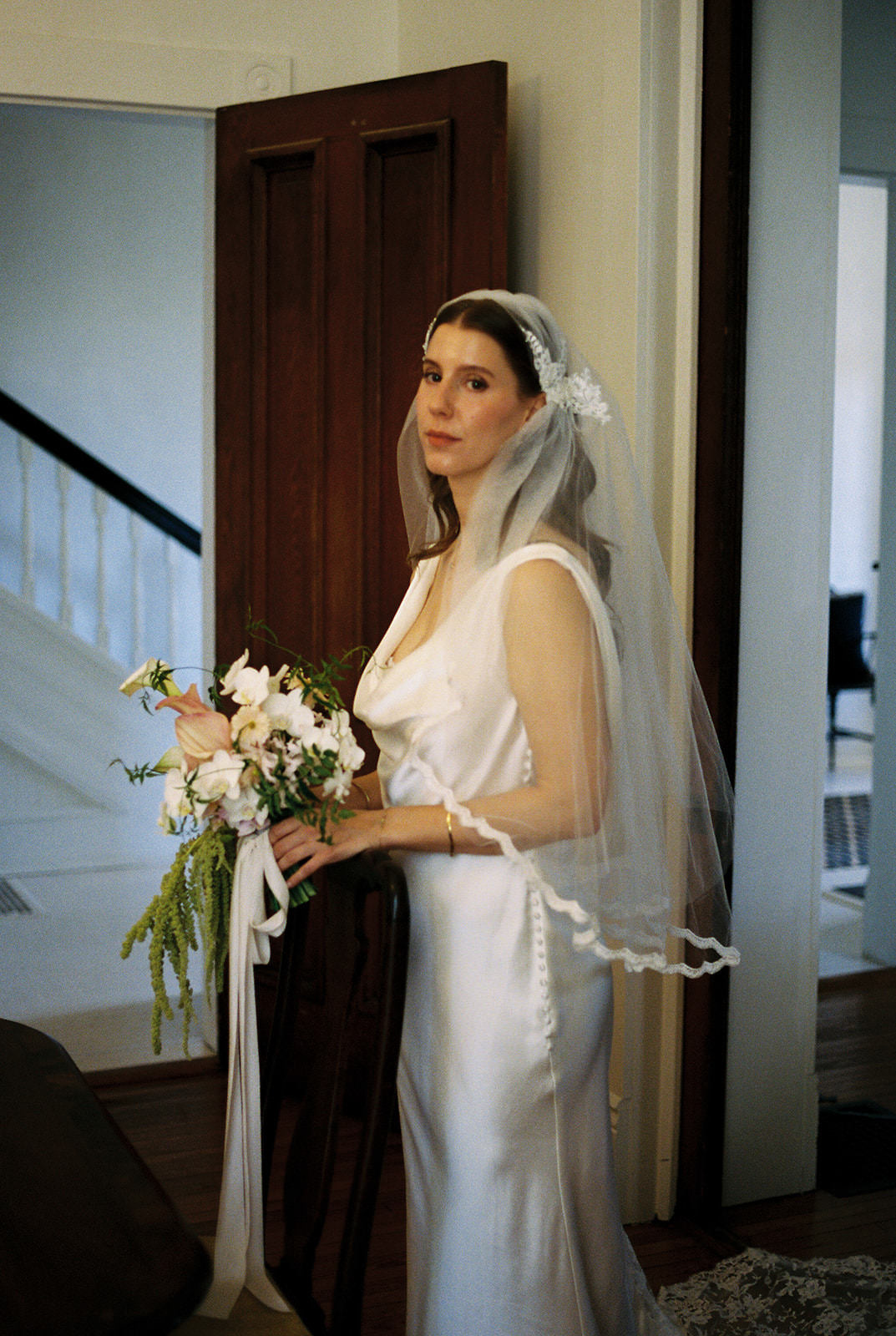 bride wearing a white draped-neck bridal gown and a Juliet cap veil with narrow scallop edging that is to fingertips and white bouquet