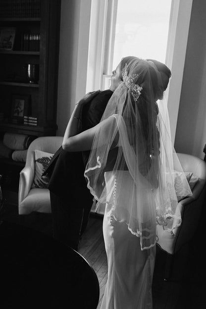 Bride wearing custom Juliet cap bridal veil from one blushing bride standing in a room with a couch and window.