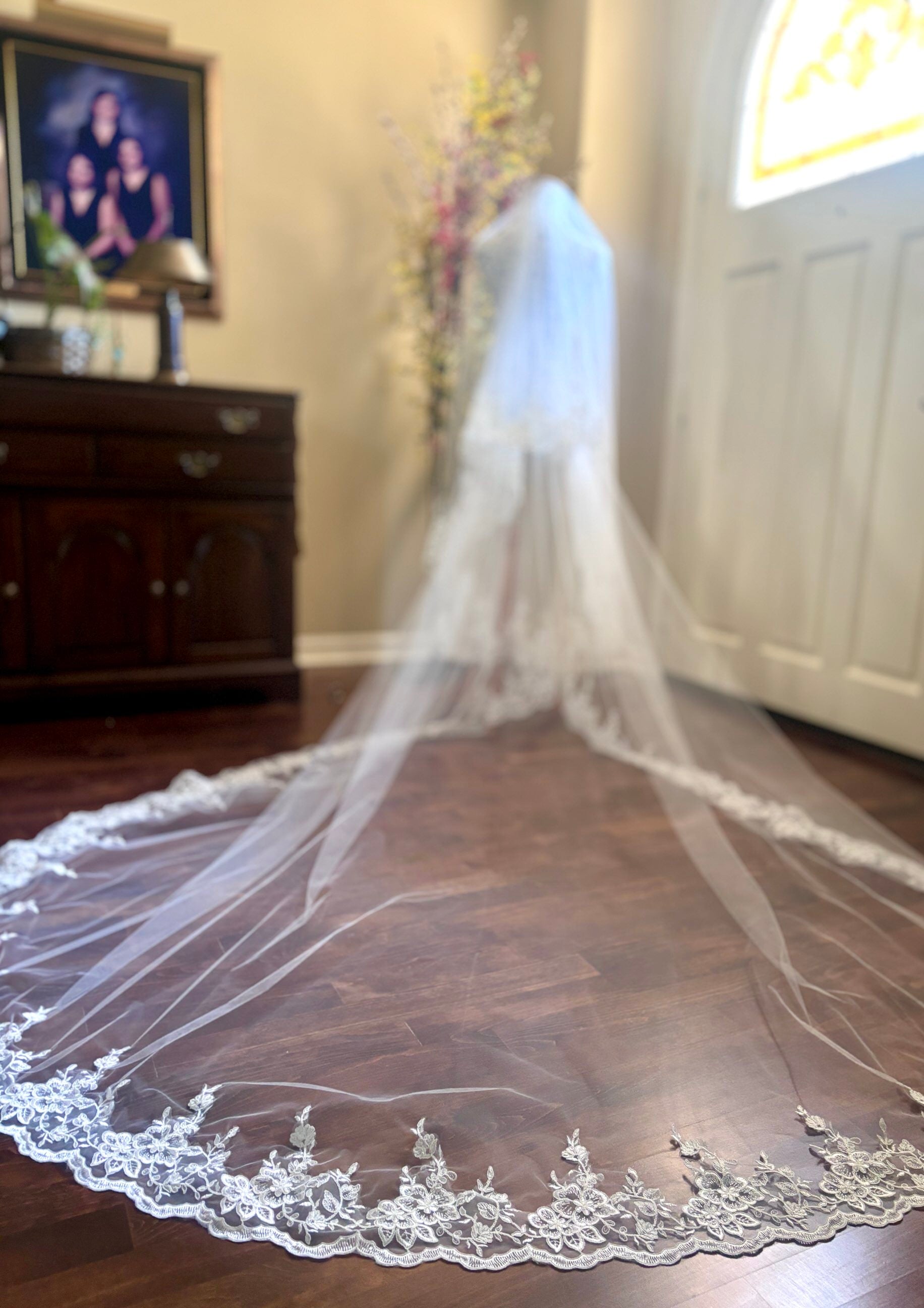 Long white  cathedral wedding veil with lace and blusher on a wooden floor.