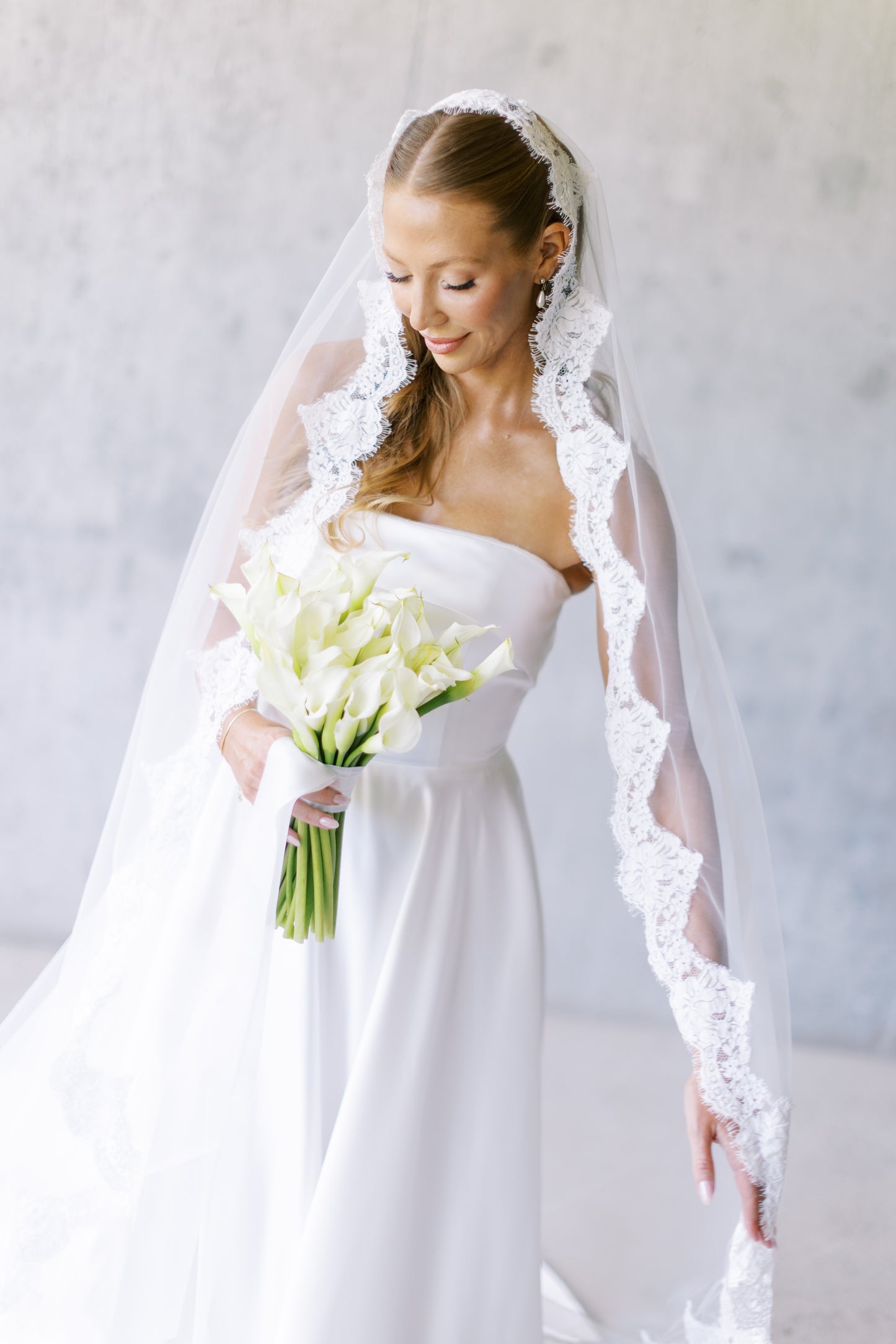 Bride in a white wedding dress with an eyelash lace veil holding a lily bouquet 