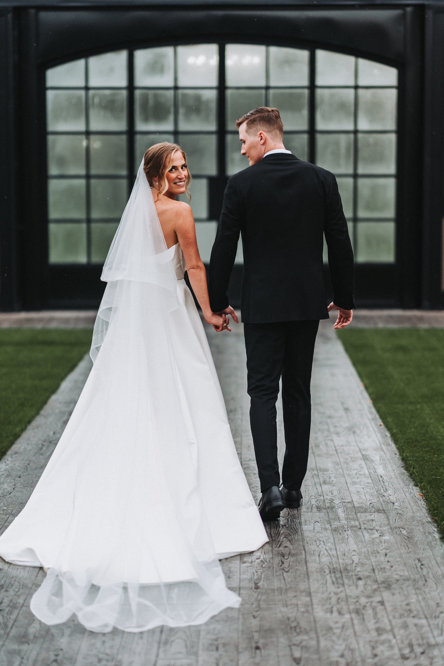 bride and groom holding hands on a pathway with a long horsehair bridal veil with blusher
