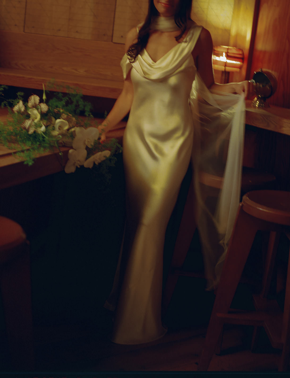 Woman in a white  draped satin sheath gown holding a sheer tulle necklace scarf around her neck
