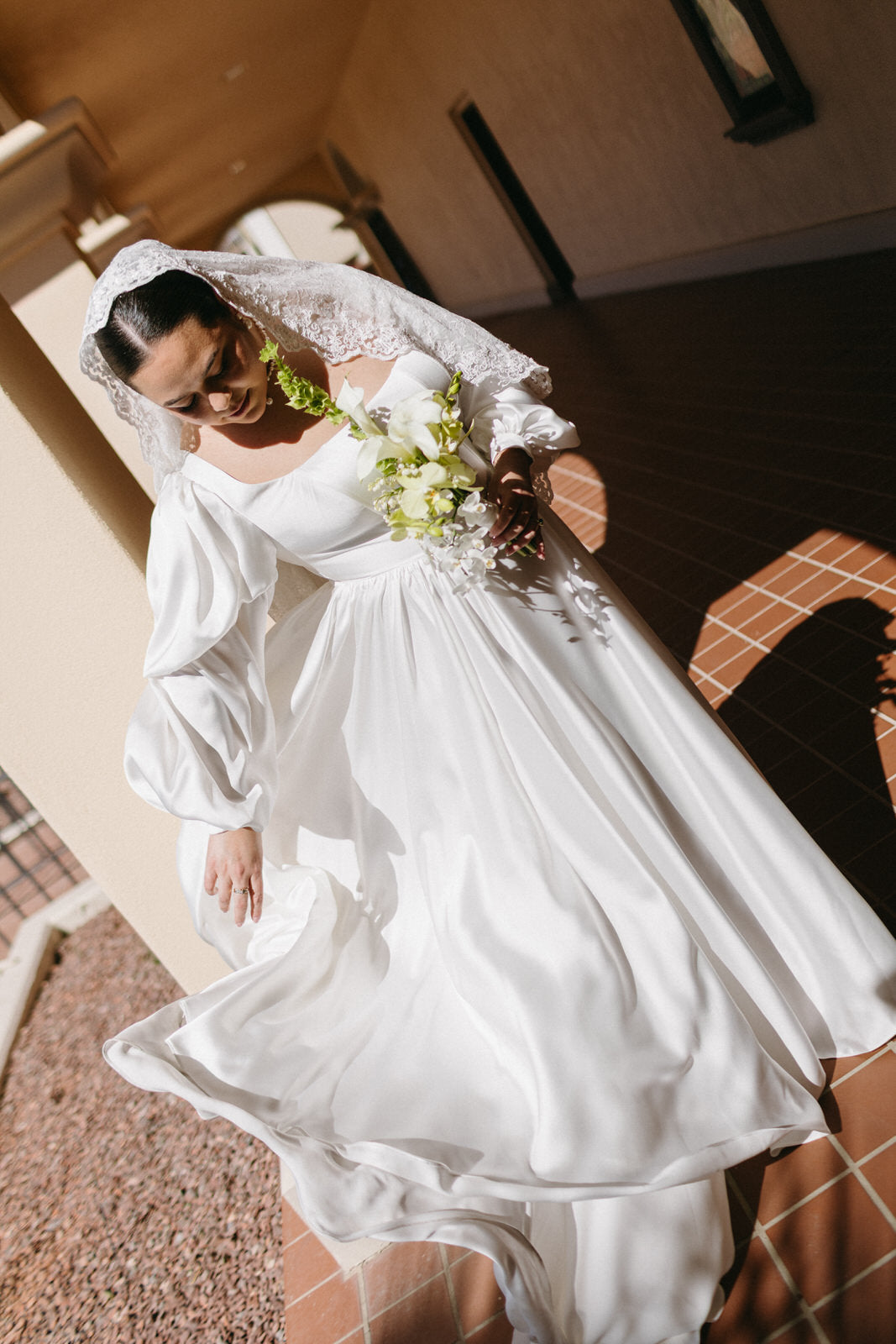 A bride in a white satin wedding dress with removable dramatic puffed sleeves and a lace veil