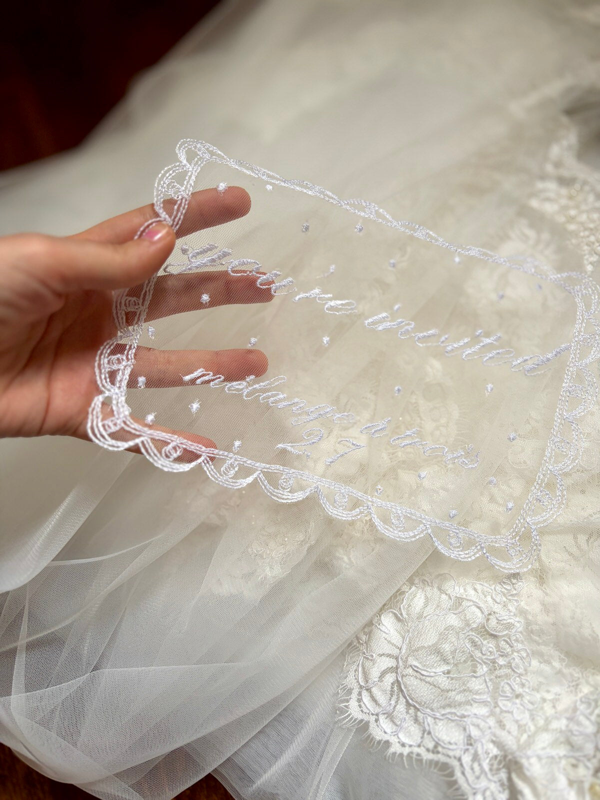 Close-up of a hand holding a piece of white embroidered fabric with personalized wedding date and location