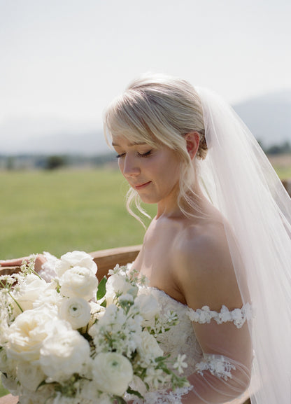 Bride holding a bouquet of white flowers wearing a simple long tulle bridal veil over bun updo chignon
