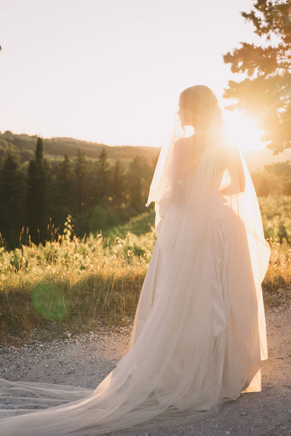 bride in a DF wedding dress standing in a Tuscany field with the sun shining through her drop cathedral length ivory wedding veil
