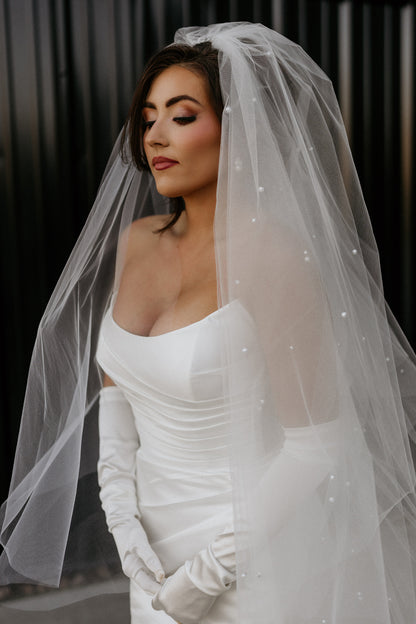 Woman in a white cat eye strapless wedding dress with a pearly puffy veil against a dark background