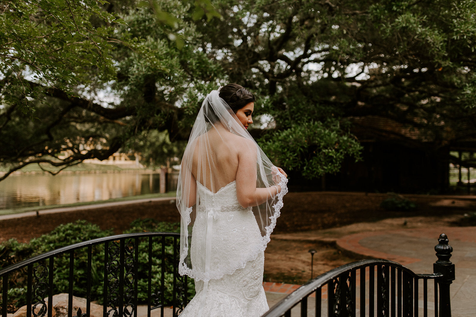 Load video: bride wearing strapless wedding dress with semi lace medium length wedding veil as she walks with her groom around her garden venue