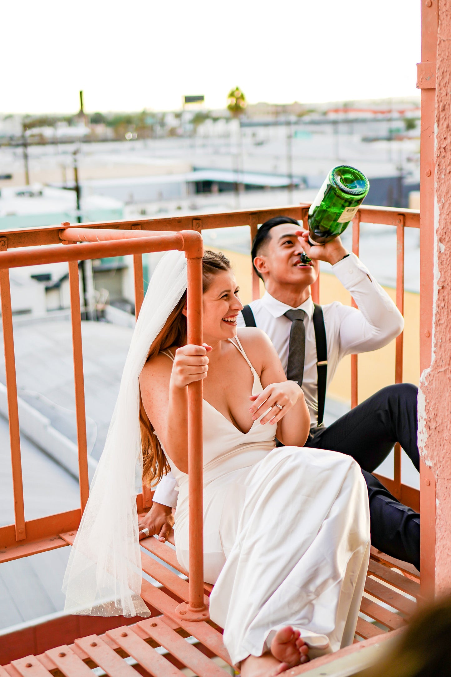 metal industrial modern wedding with bride wearing waist length dotted Point d' Esprit bridal veil and laughing as groom drinks beer