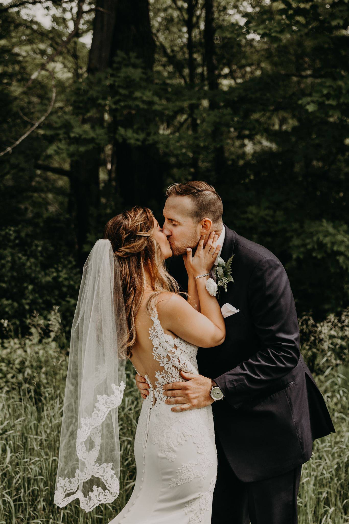 whimsical organic French lace trim wedding veil in braided half up half down bridal hairstyle on bride kissing groom