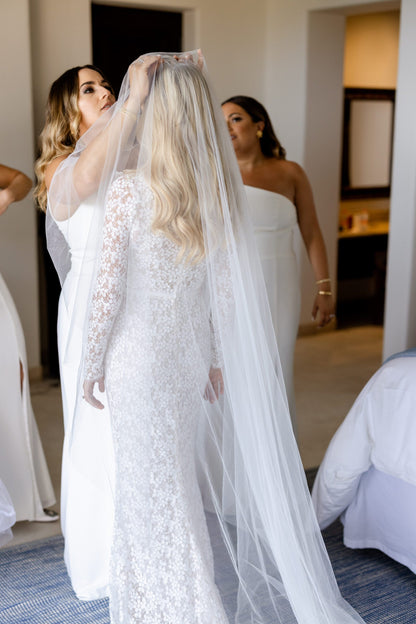 bridesmaid putting in veil hair comb attached to long cathedral veil and bride wearing long sleeved wedding dress