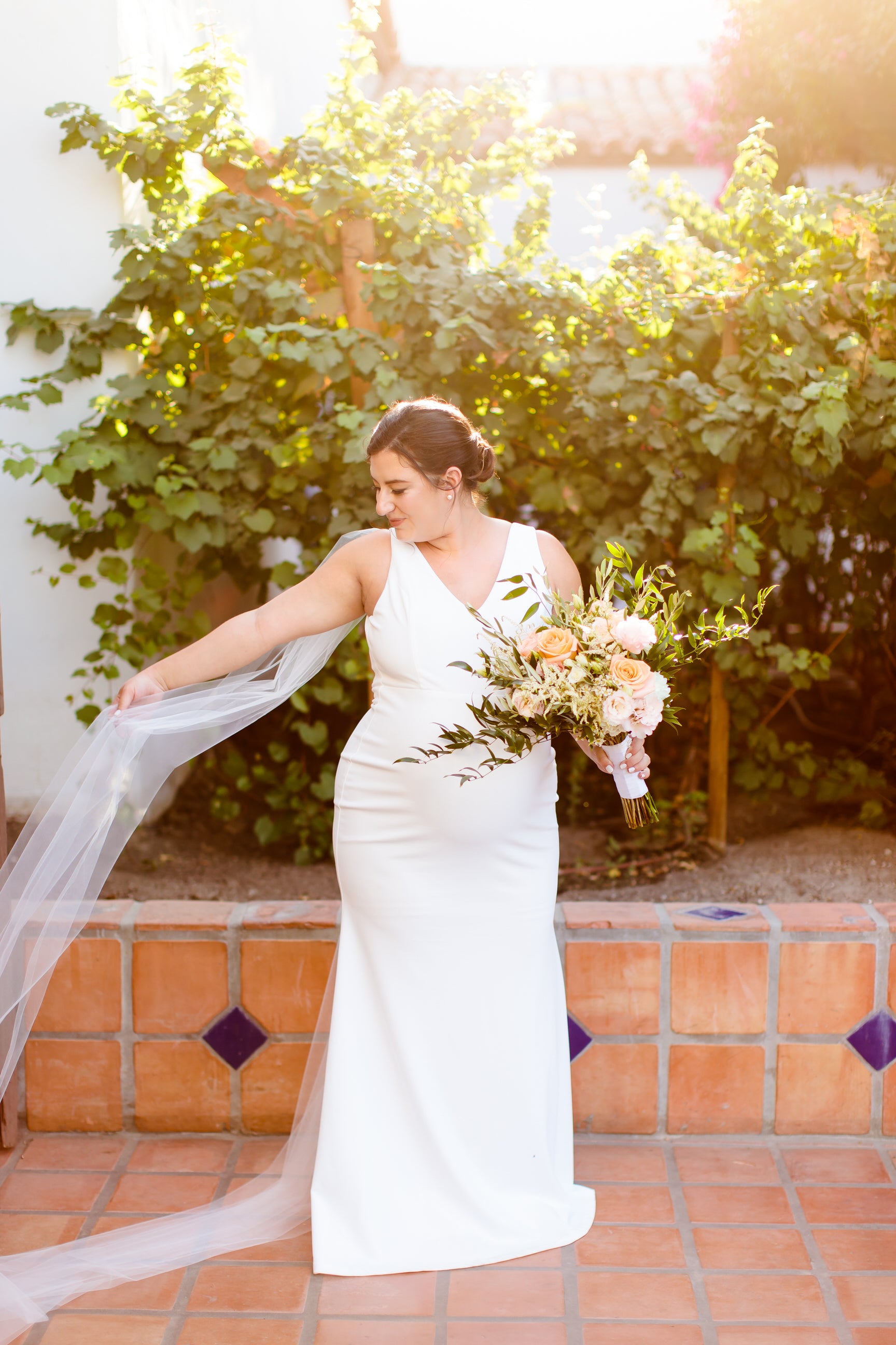 simple crepe gown on pregnant bride with bridal cape veil shoulder wings and blush and orange rose bouquet